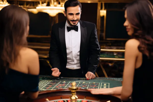A professional dealer in a tuxedo greeting players at the roulette table, symbolizing the authentic live casino feel at SPINARA.