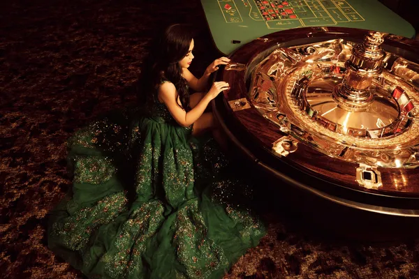 SPINARA — A high-class gaming experience without limits A woman in a luxurious green gown next to an ornate roulette wheel, capturing the upscale casino mood of SPINARA.