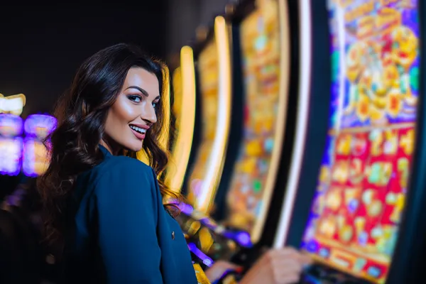 SPINARA Slots — Thousands of thrilling machines await A woman smiling by bright slot machines showing lucky symbols, showcasing the exciting slot offerings at SPINARA.